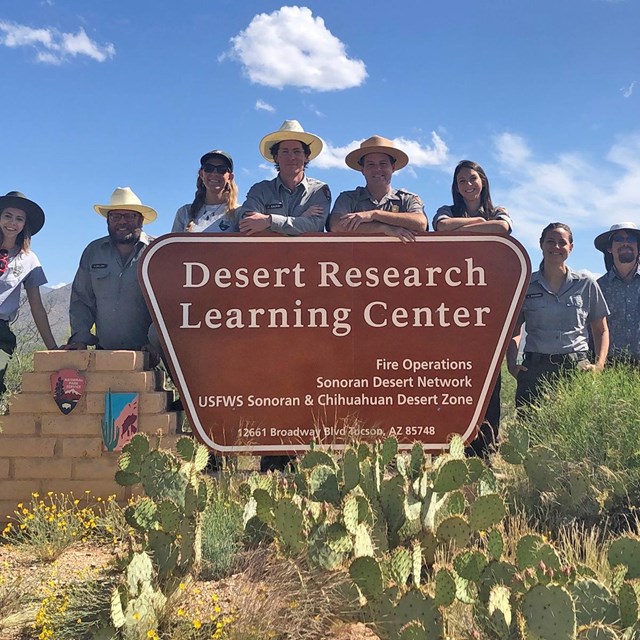 People in NPS uniform gather around a sign for the Desert Research Learning Center