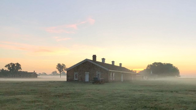 A stone building in a grassy area covered in morning fog at Fort Larned National Historic Site.