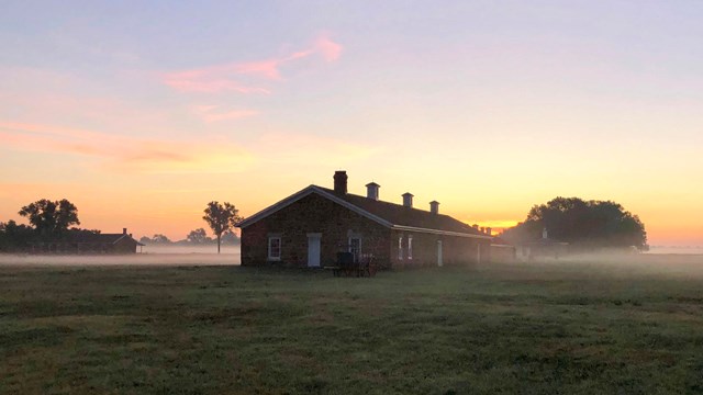 A stone building in a grassy area covered in morning fog at Fort Larned National Historic Site.