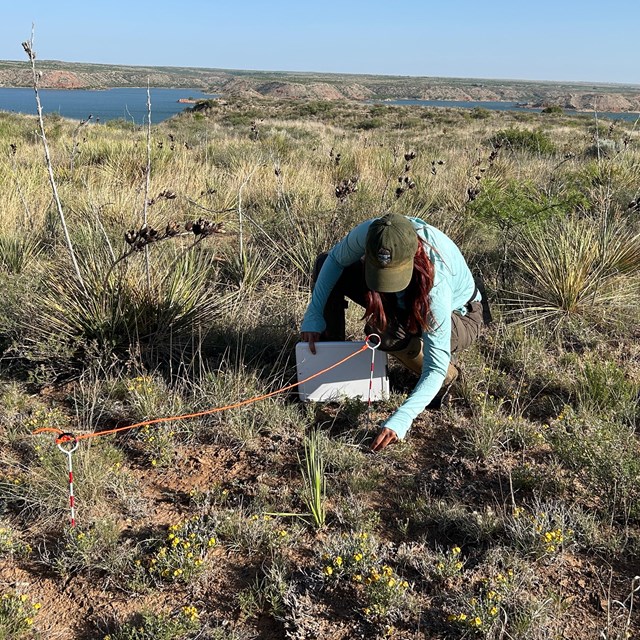 A person crouching down holding a clipboard next to two spikes connected with a rope.
