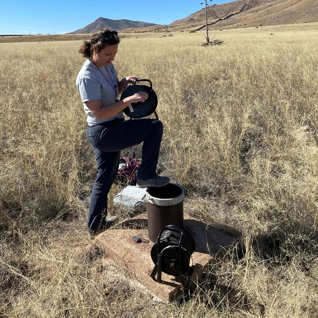 A scientist lowering a wire into a groundwater well.