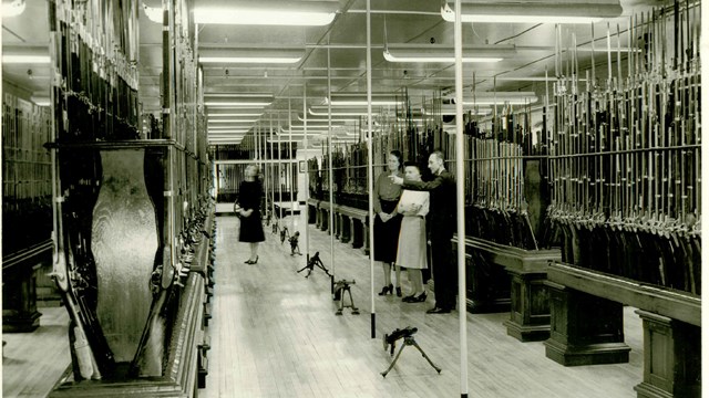 A black and white photo of rows of muskets in the armory arsenal. 