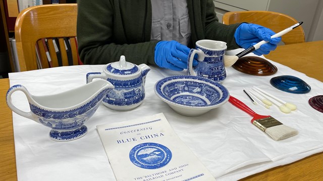 A Ranger wearing gloves carefully cleaning historic pieces of china