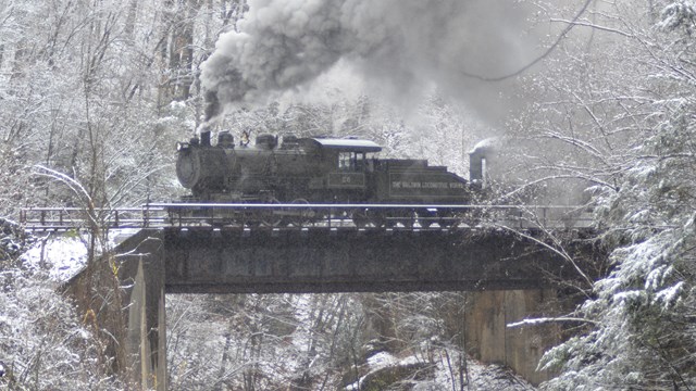 Small steam engine atop a bridge in a snowy landscape 