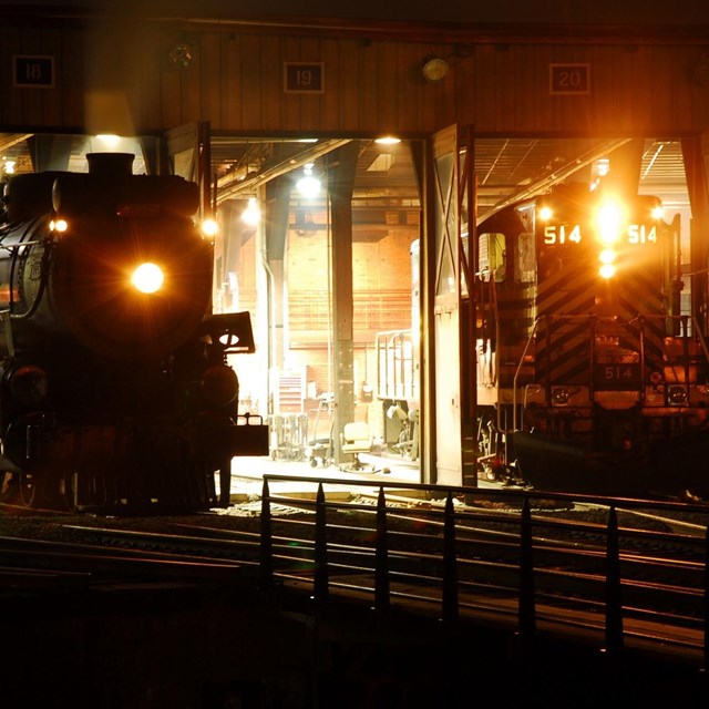 two locomotives parked in roundhouse at night