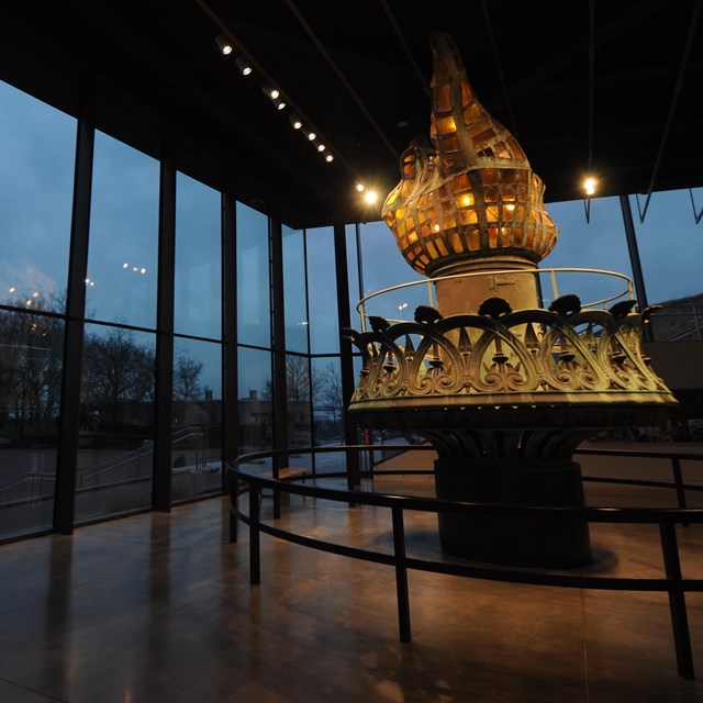A view from inside the museum at dusk. The original torch is lit on the left of the image.