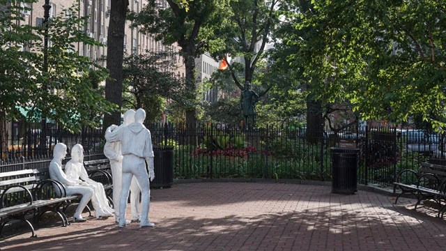 Christopher Park, surrounded by green benches, laid with brick, with two white statues in the center