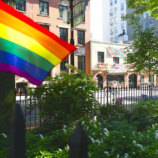 A brick facade in the background, with a rainbow flag in the foreground.