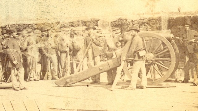 A black and white photo of a cannon on a wooden platform, with soldiers and another cannon on a plat