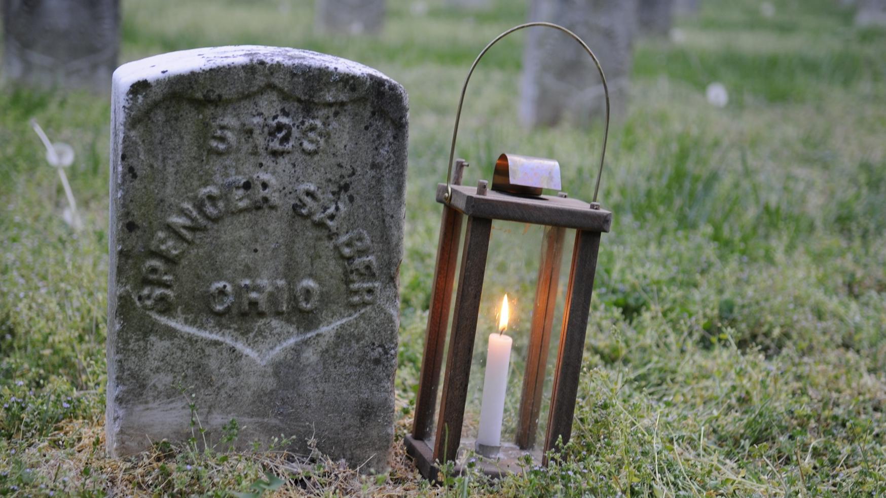 Gravestone with text reading S123 Spencer Sable Ohio and lantern with lit candle to the right