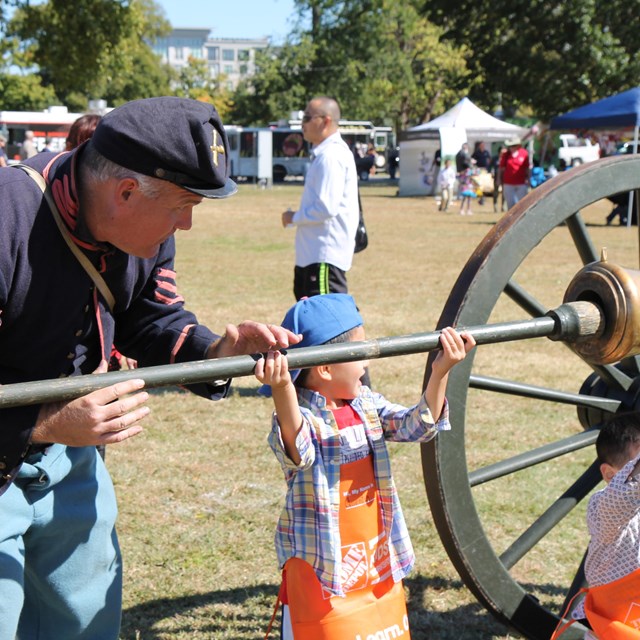 A living historian in a Union uniform and a child push a rammer into a Civil War cannon.