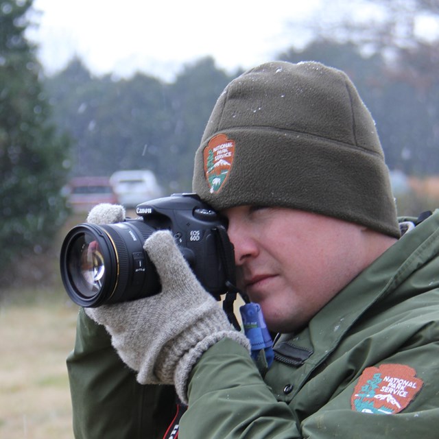 A park ranger holds a camera to his eye.