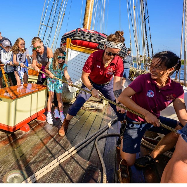 A group of people help pull lines on a tall ship.