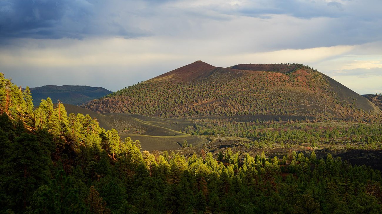 sunset crater volcano rises from a basalt lave field under a monsoon sky