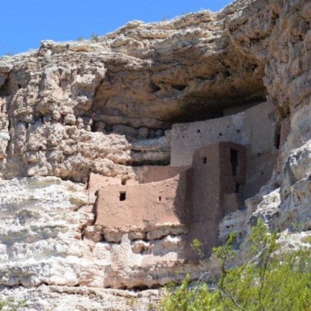 A five-story cliff dwelling in a limestone bluff, with green tree tops visible at the bottom