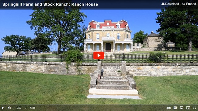 Uniformed female park ranger looks toward camera in front of large historic building.