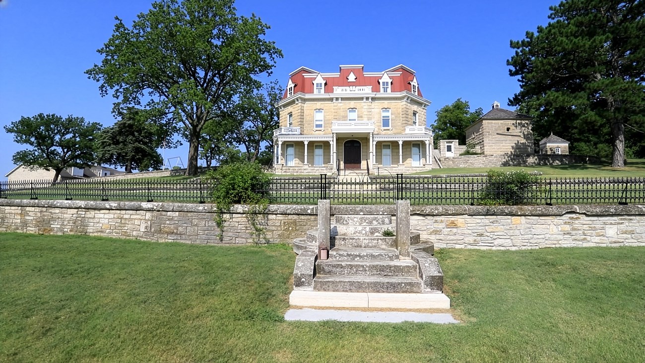Uniformed female park ranger looks toward camera in front of large historic building.