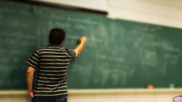 Teacher writing on a chalk board. 