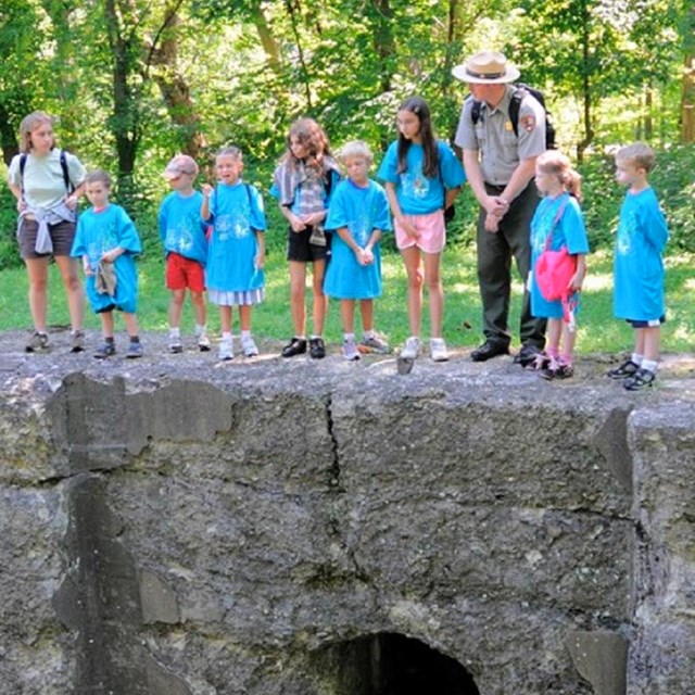 Young students with NPS ranger standing on stone lock. 