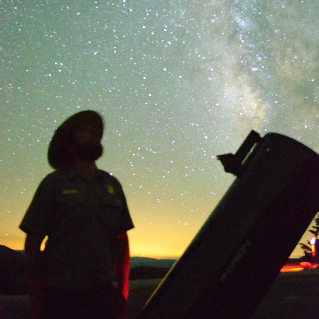 Ranger next to a telescope at night