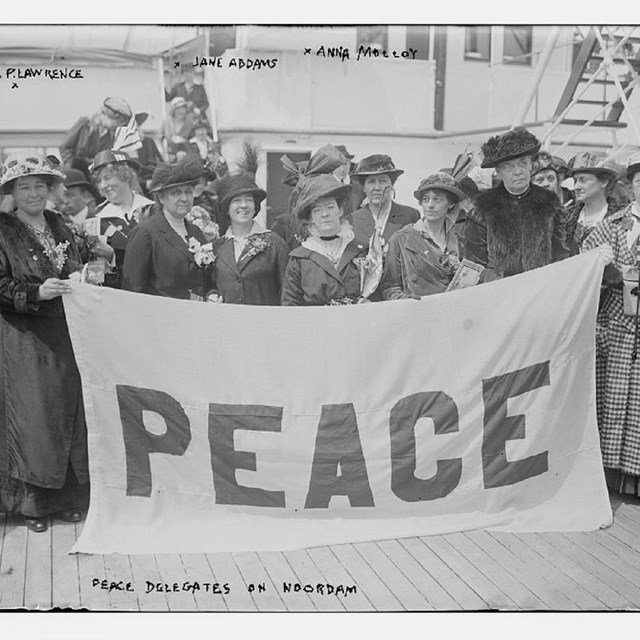 A group of women standing on the deck of a ship holding a banner reading Peace