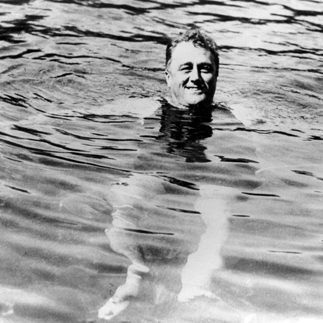 FDR in a swimming pool. His head is above the water and his legs are visible.