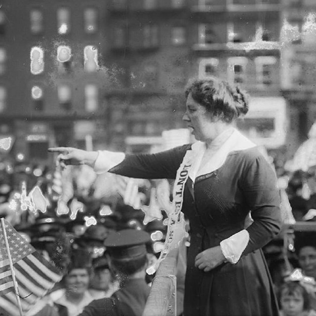 Black and white photo of a woman pointing to a crowd.