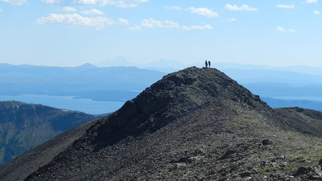 Hikers standing on the rocky top of Avalanche Peak with Yellowstone Lake in the background.
