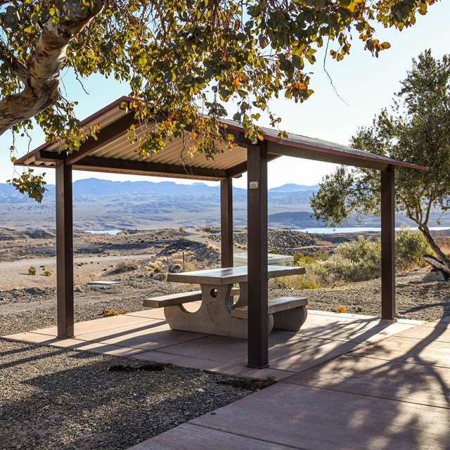 A shaded picnic table with a mountainous landscape in the background.