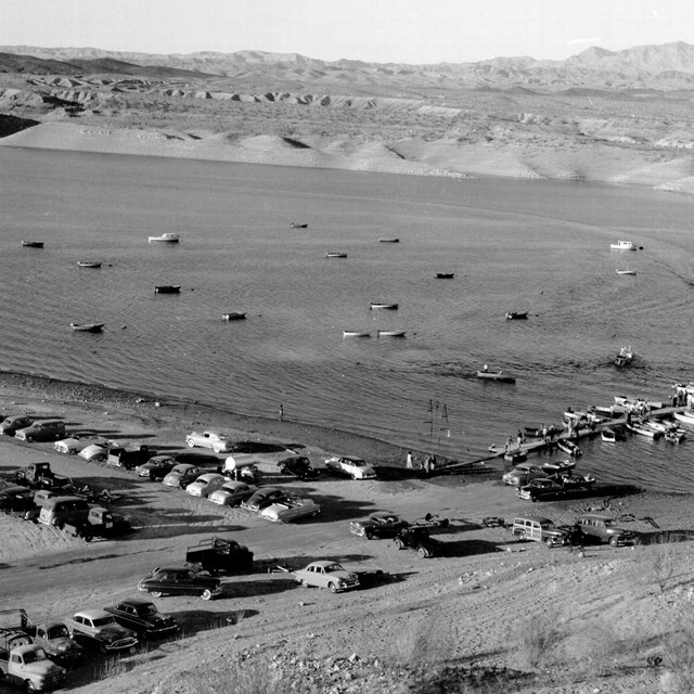 A historical photo showing a large body of water and a beach with several cars parked.