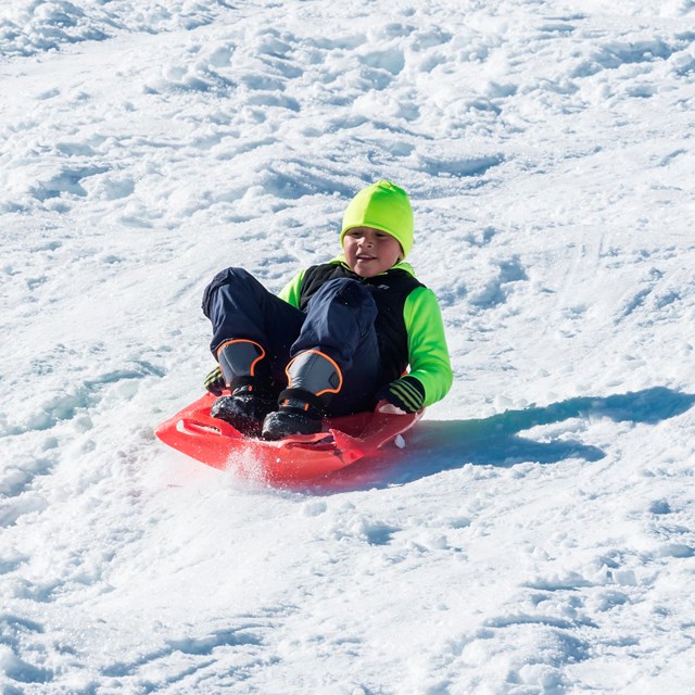 A young boy sleds down a snowy hill.