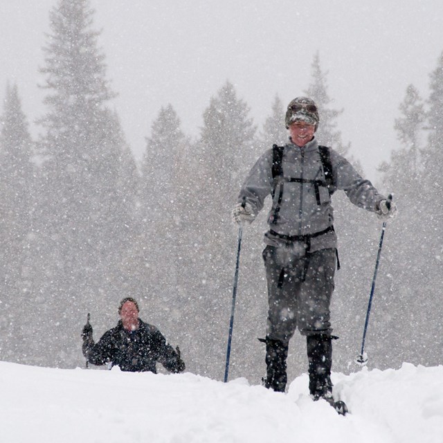 Two cross country skiers appear over a small hill during a snow storm.