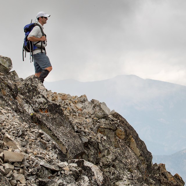 Male day-hiker standing atop a rocky mountain.