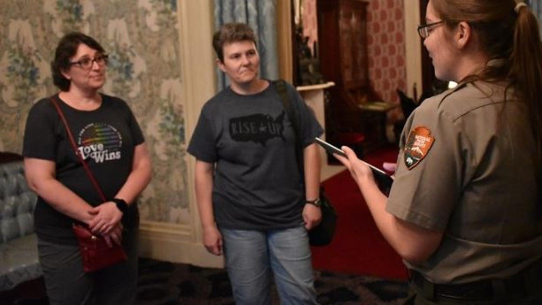 Two women are standing in a room while a ranger gives a tour.
