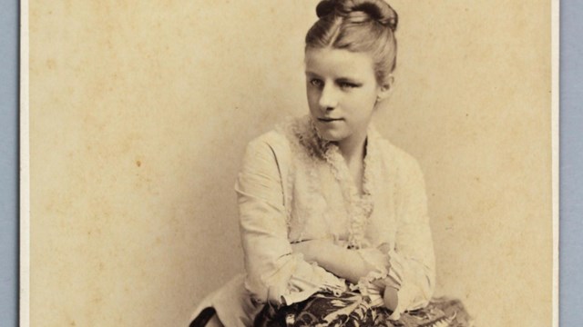 Sepia portrait of Corinne leaning over against an object, gazing down and off in distance