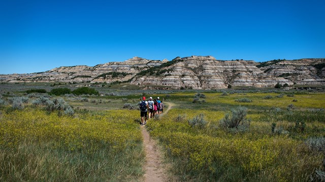 A family follows a flat, dirt trail towards a row of buttes.