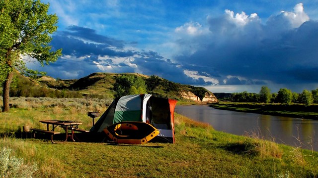 A tent with inflatable canoe on the edge of the Little Missouri River.