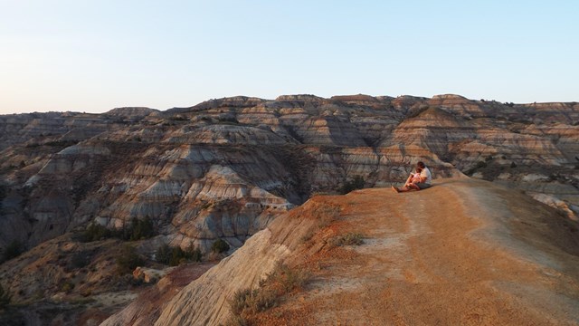 A man and child sit on a butte, with a sweeping view of the badlands behind them.