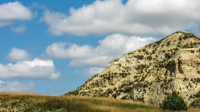 A butte in the right half of the photo, with a blue sky and rolling grassland.