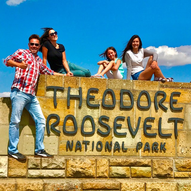A smiling family poses atop the park's stone entrance sign.