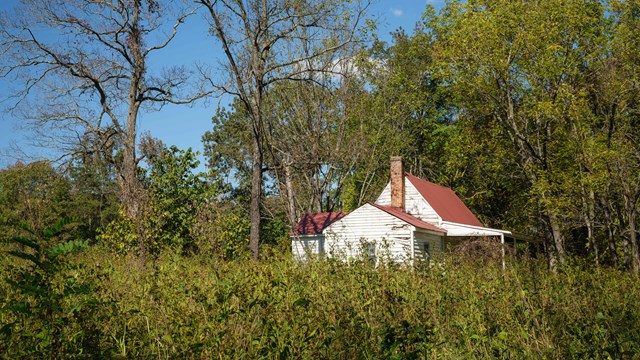 White tenant house with red roof, surrounded by vegetation and nature trail