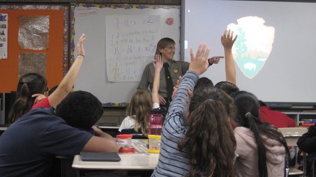 Ranger pointing at children with hands raised in a classroom