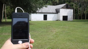 an audio tour device held by hand with historic barn in distance