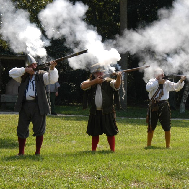3 people in costume shooting muskets