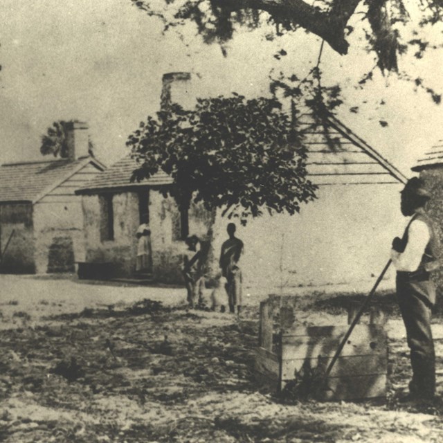 a sepia tone image of a man in front of the tabby cabins with roofs