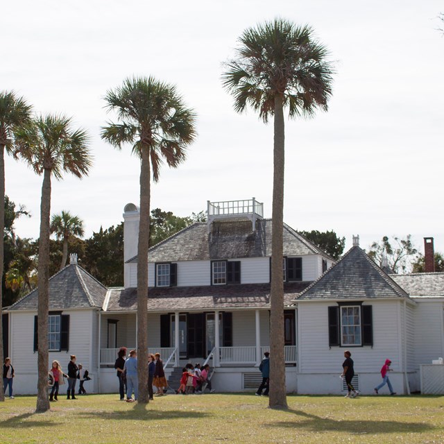 a two story white historic building with palm trees in front 