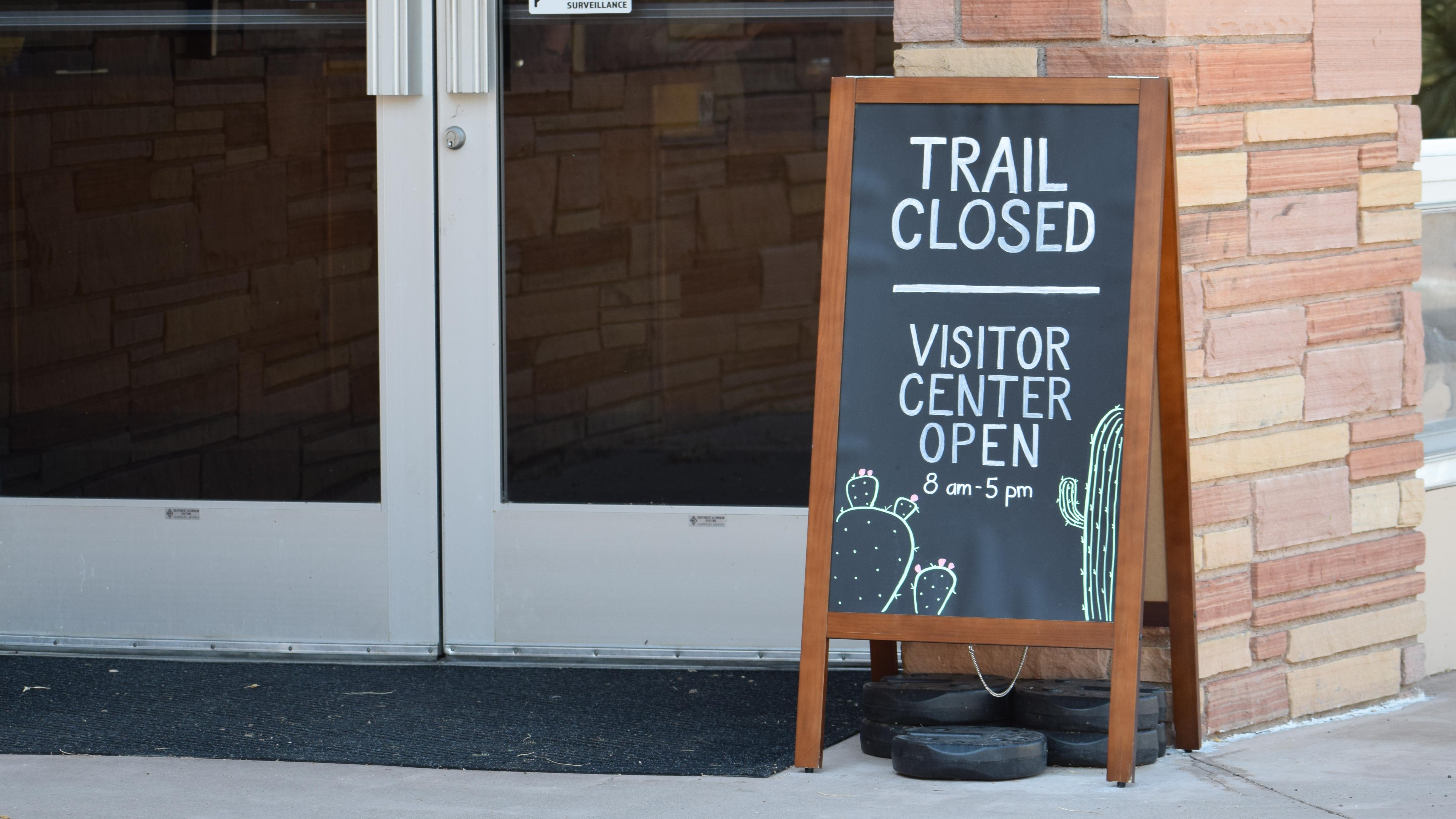 Photo of glass doors with a sign in front of it that says "Trail Closed."