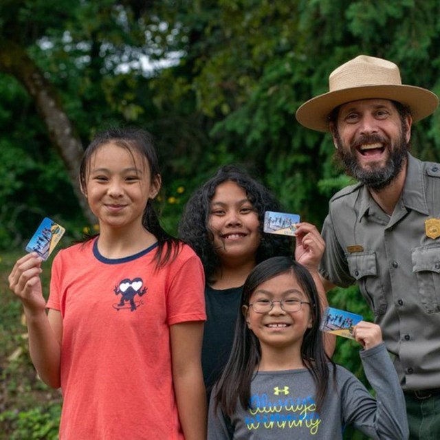 three kids hold up every kid outdoors passes while standing next to a smiling ranger