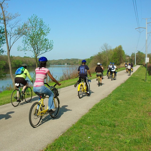 Group riding bikes on paved path next to body of water