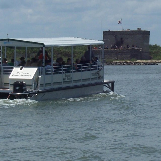 a ferry on water driving toward a fort in the distance